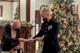 man in uniform in front of Christmas tree giving a paper to a senior